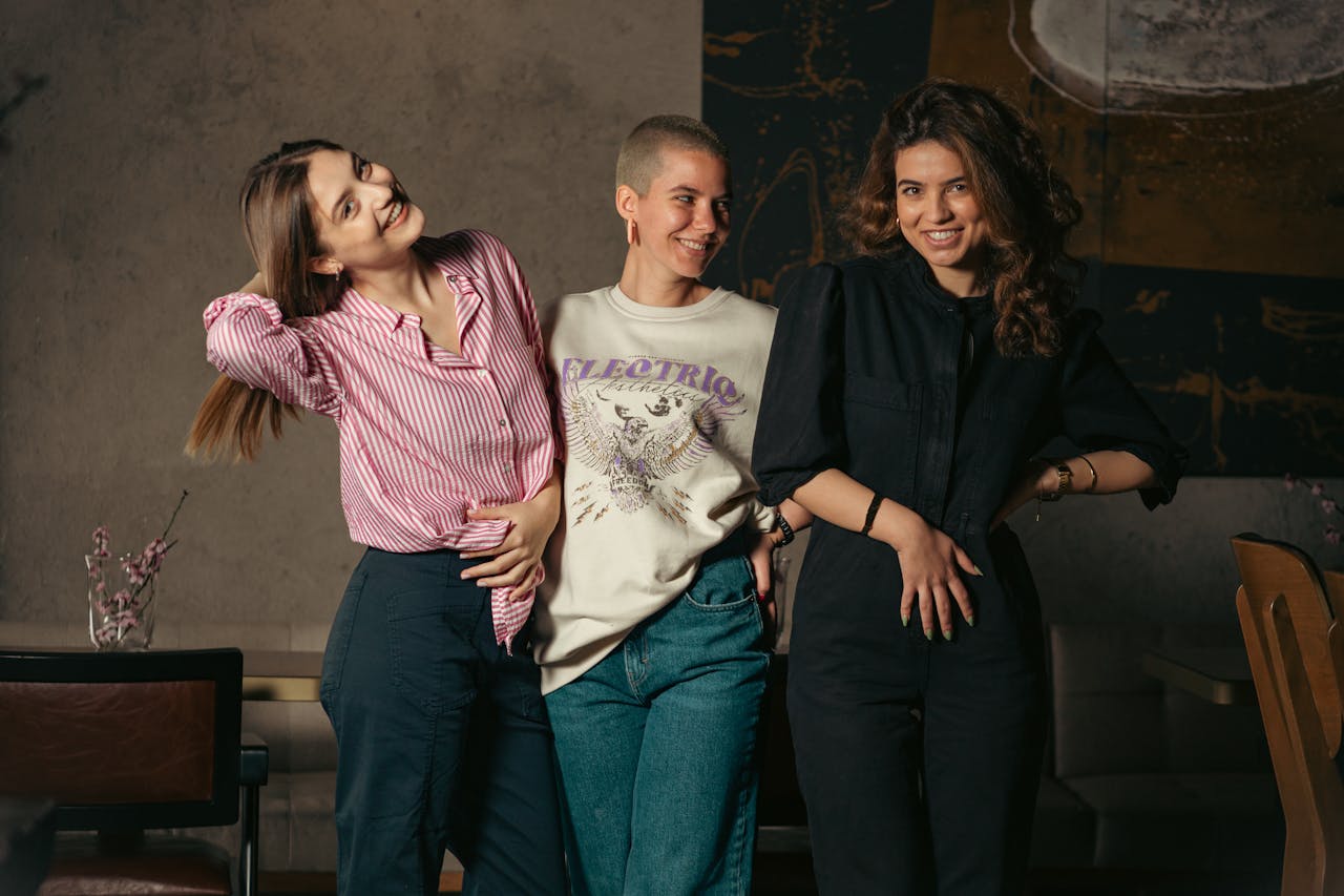 A group of three diverse women smiling and posing indoors, exuding a sense of friendship and joy.