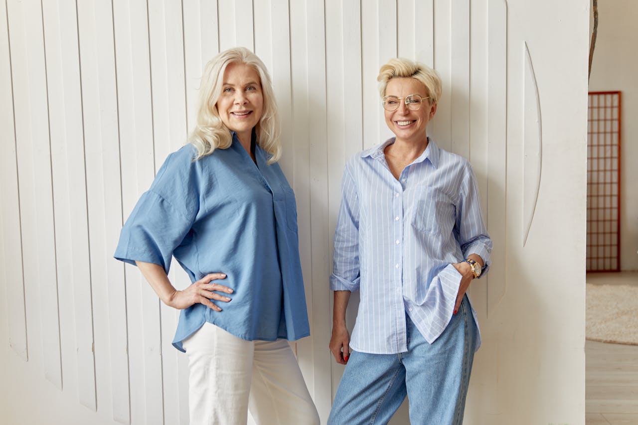 Two blonde women smiling in casual blue outfits, standing indoors. Perfect for themes of friendship and lifestyle.